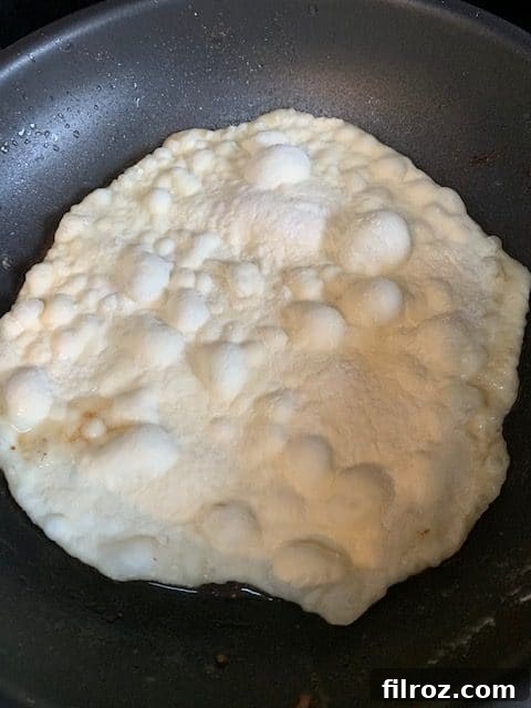 Naan dough being rolled out with a rolling pin.