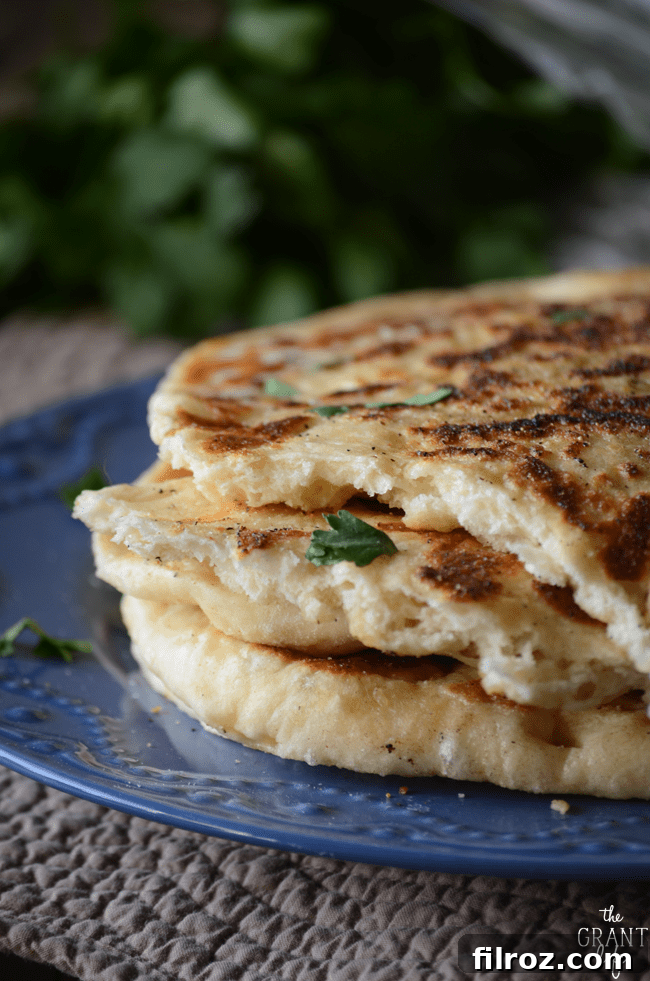 A stack of perfectly cooked homemade naan bread, garnished with fresh cilantro.