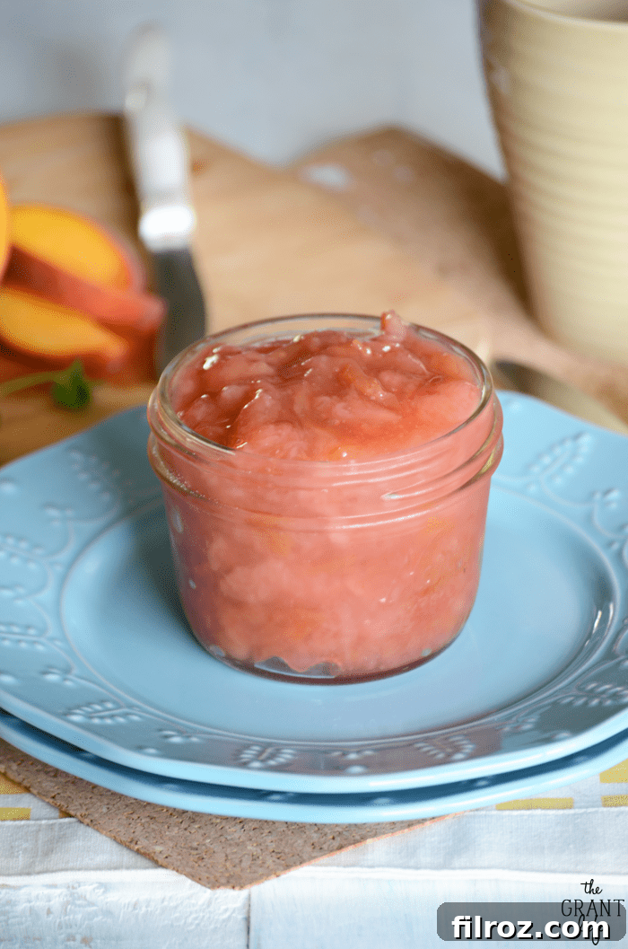 Jar of homemade peach jam with fresh peaches and leaves