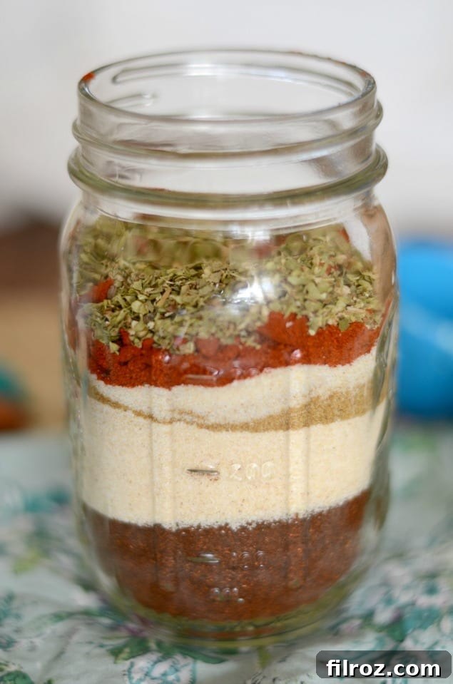 Make Your Own Taco Seasoning 2 A glass jar filled with layers of various spices, representing homemade taco seasoning mix, with a rustic background.
