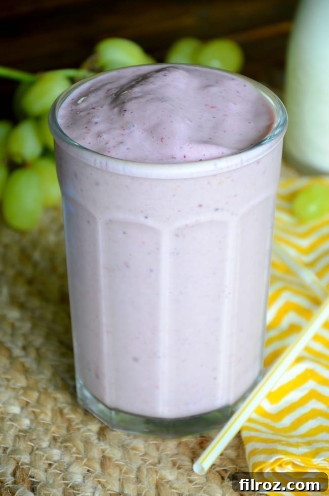 A vibrant triple berry smoothie in a glass with berries scattered around.