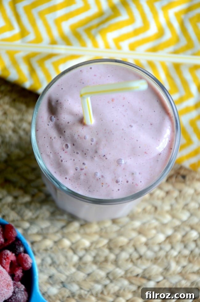 Close-up of a child's hand holding a glass of a berry smoothie.
