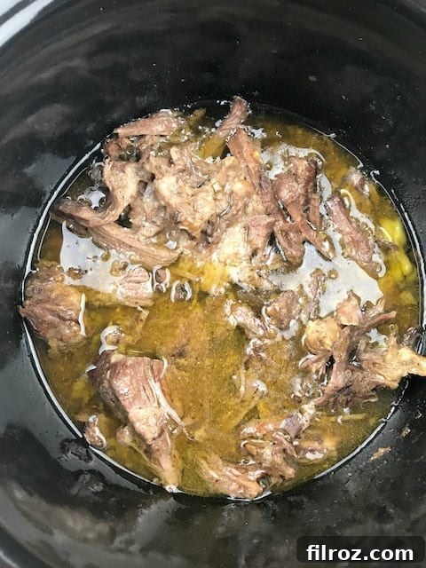 Mississippi Pot Roast cooking slowly in the crock pot, surrounded by its flavorful sauce.