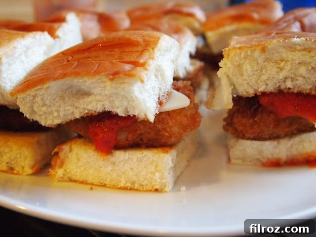Assembled chicken parmesan sliders with melted cheese and top buns on a griddle.