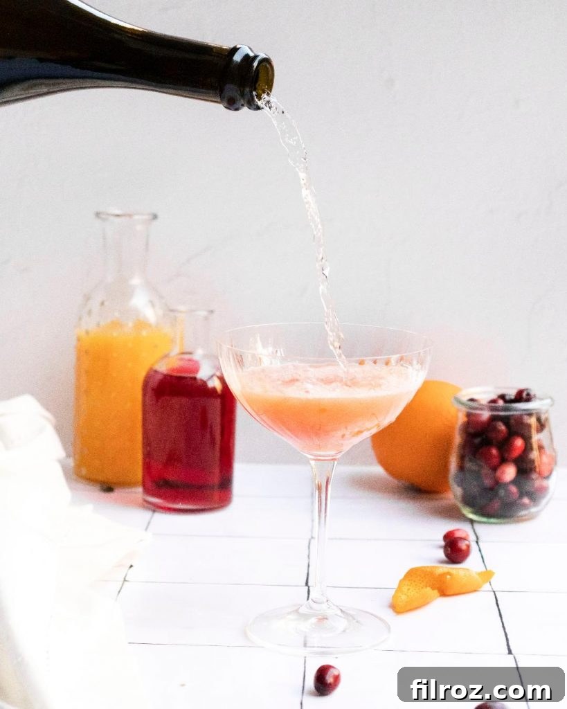 Hand pouring cranberry orange mimosa into a flute glass