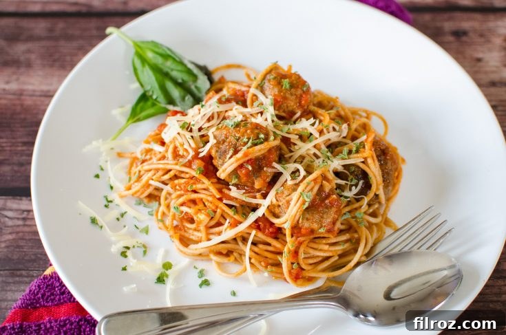 Spaghetti and meatballs dish on a white plate with cutlery, ready to eat.