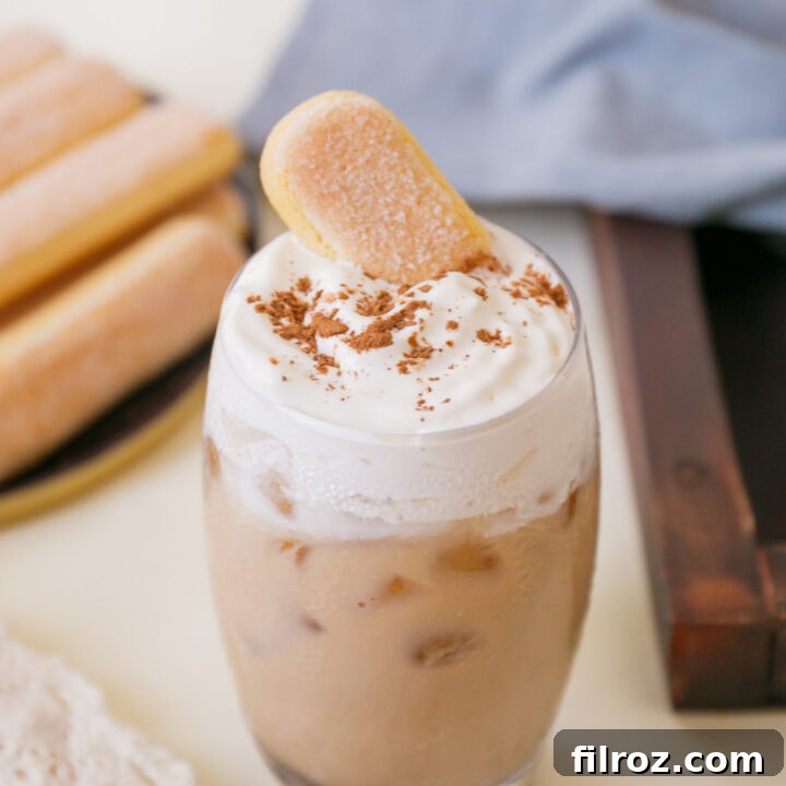 A beautifully presented iced tiramisu latte in a clear glass, ready to be enjoyed, highlighting its creamy layers and a ladyfinger garnish.